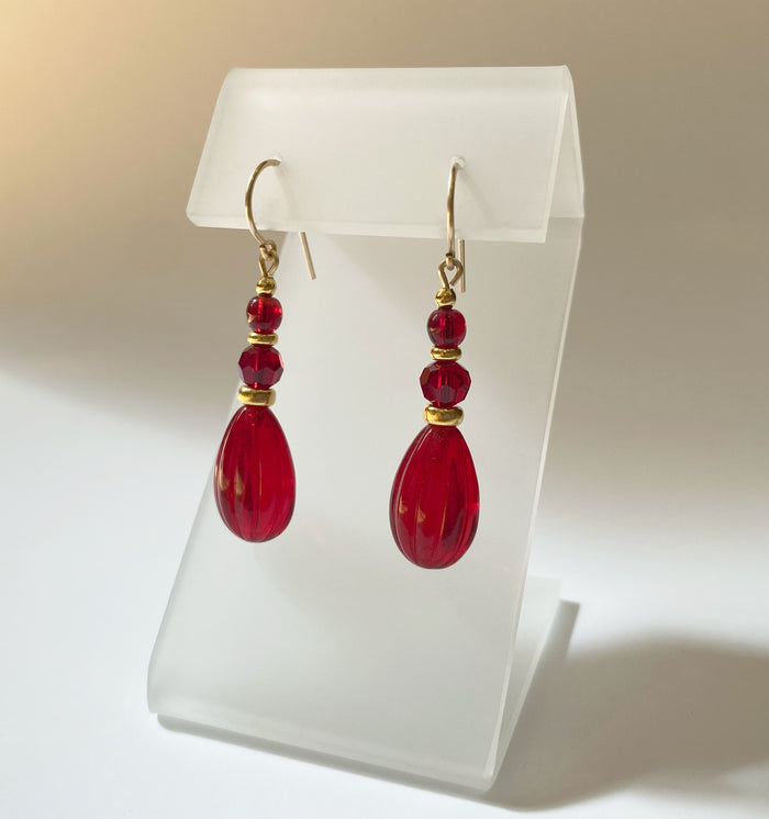 Red glass and gold dangle earrings from Owen Glass Collection with intricate design, hanging gracefully on display.