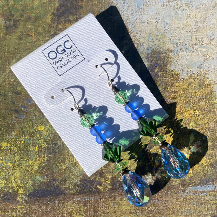 Iridescent light sapphire crystal earrings from Owen Glass Collection with bronze-tone hooks, showcasing shimmering gemstone details.