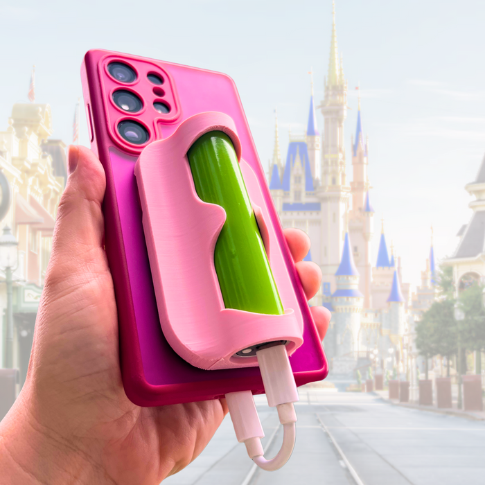 A hand holds a magic sidekick magnetic power bank sleeve from parks and prep co with a power bank inserted while charging at a theme park